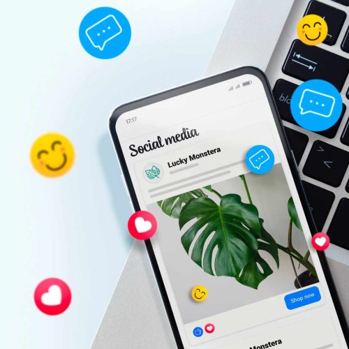 Smartphone displaying social media post with a Monstera plant image beside a keyboard. Floating emojis convey a lively, engaging social media vibe.